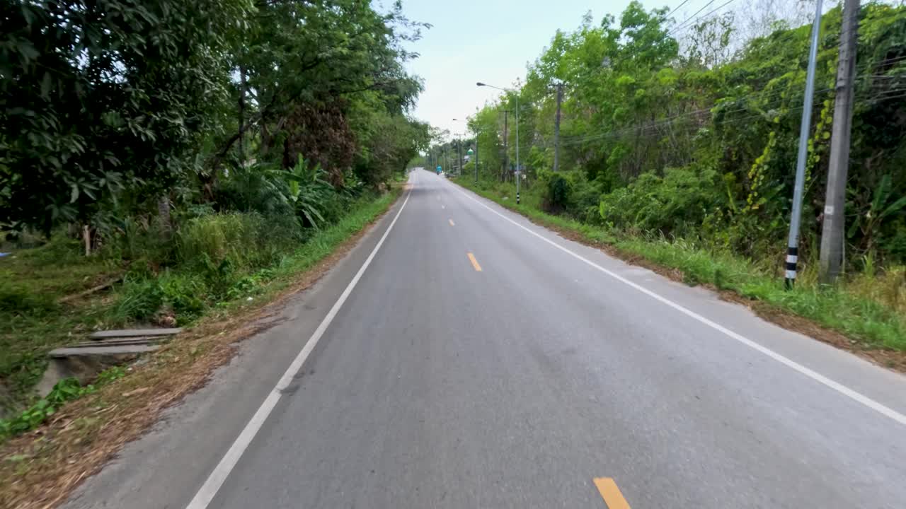 Smooth daytime drive along quiet rural road, passing rubber trees, greenery, and small village houses