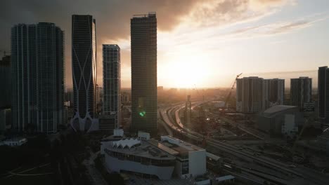 Panorama-Drohnenaufnahme-Der-Innenstadt-Von-Miami-Bei-Sonnenuntergang,-Wolkenkratzer-Im-Geschäftszentrum-Von-Florida-Und-Verkehr-Auf-Der-Autobahn,-USA