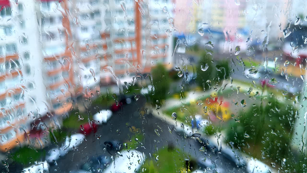 Window glass covered with drops of rain. View of the residential area blurred at backdrop.