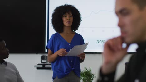 Mixed-race-businesswoman-giving-presentation-to-diverse-group-of-colleagues-in-meeting-room