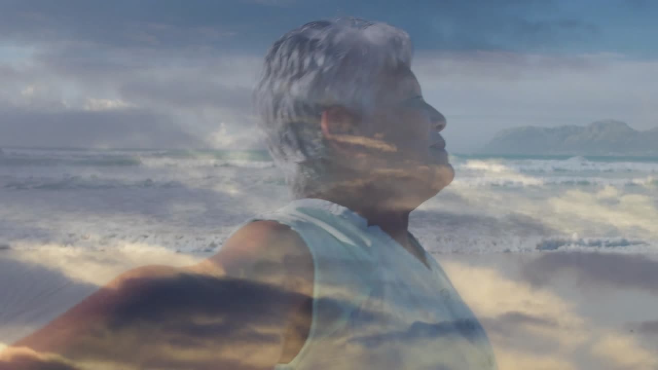 Ältere Frau greift mit Smartphone, filmt die Küste, während sich Wolken über dem Reiseprofil vermischen.