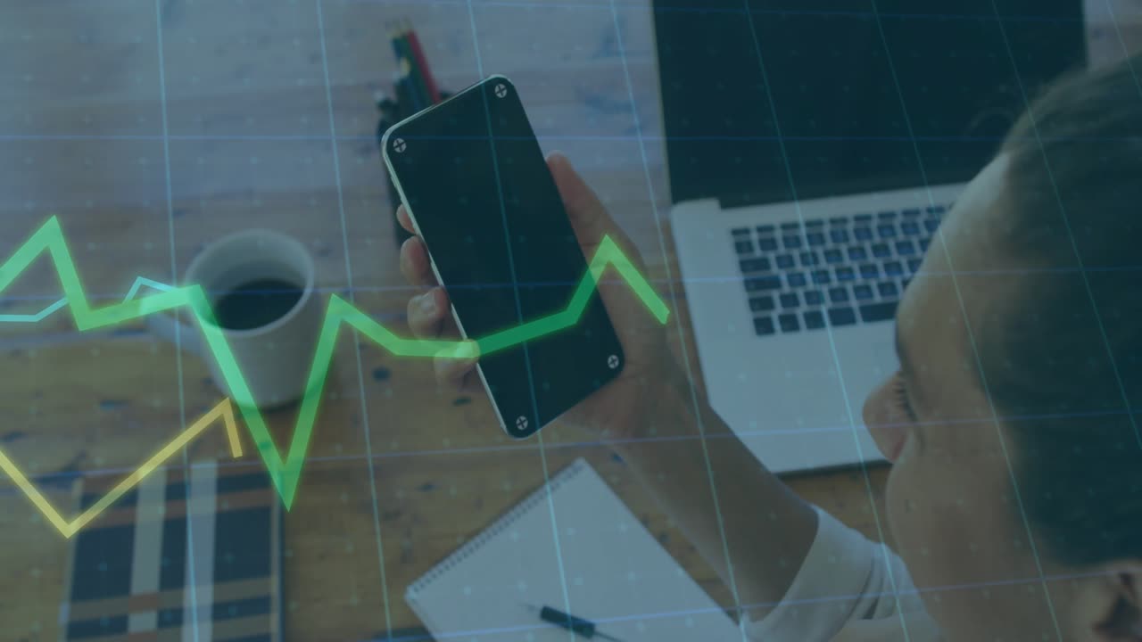 Moden kvinde tager en smartphone og studerer, mens animerede finansielle diagrammer bølger hen over skrivebordet.