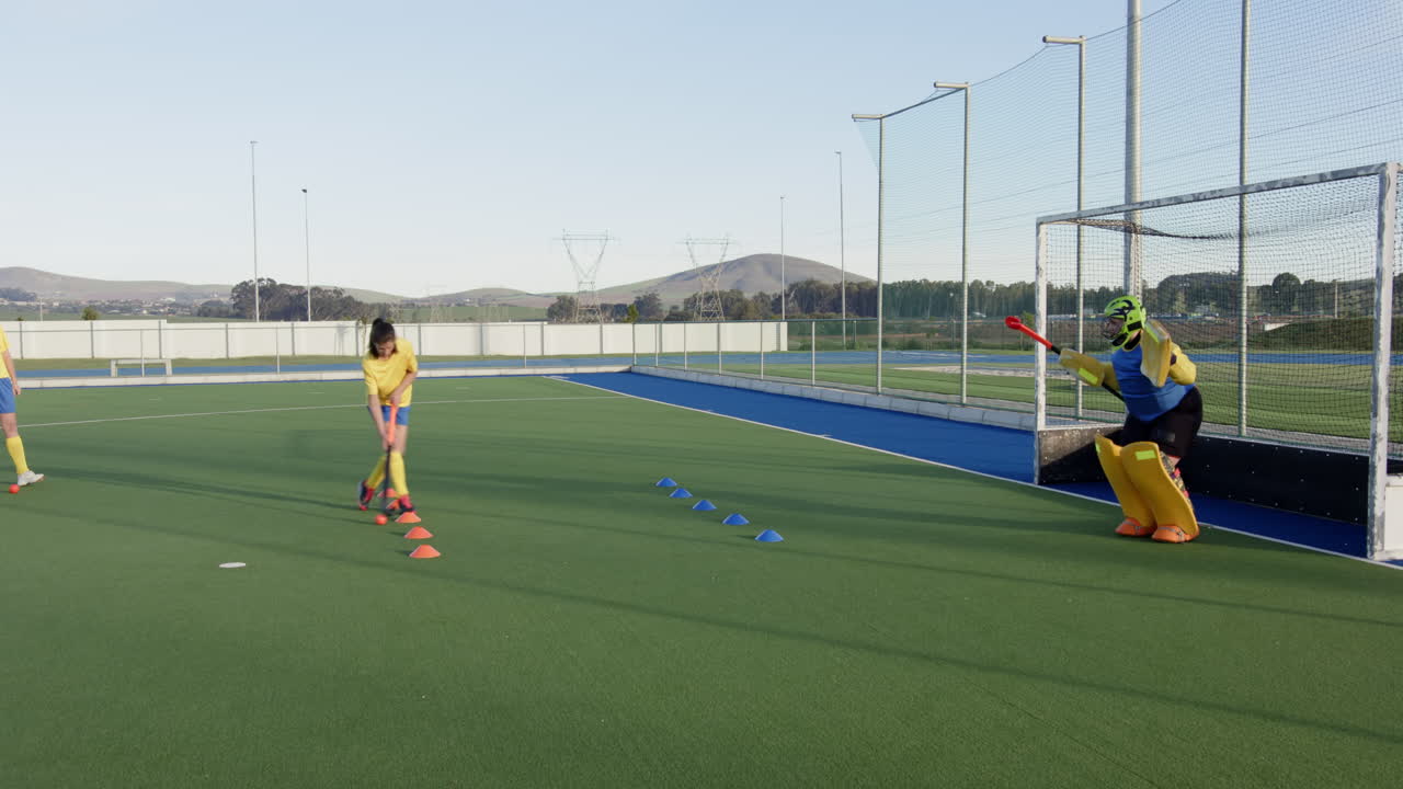 Female hockey player practicing shots on goal with focused goalkeeper defending