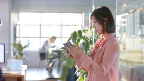 thoughtful asian businesswoman using tablet at sunny office, copy space, in slow motion