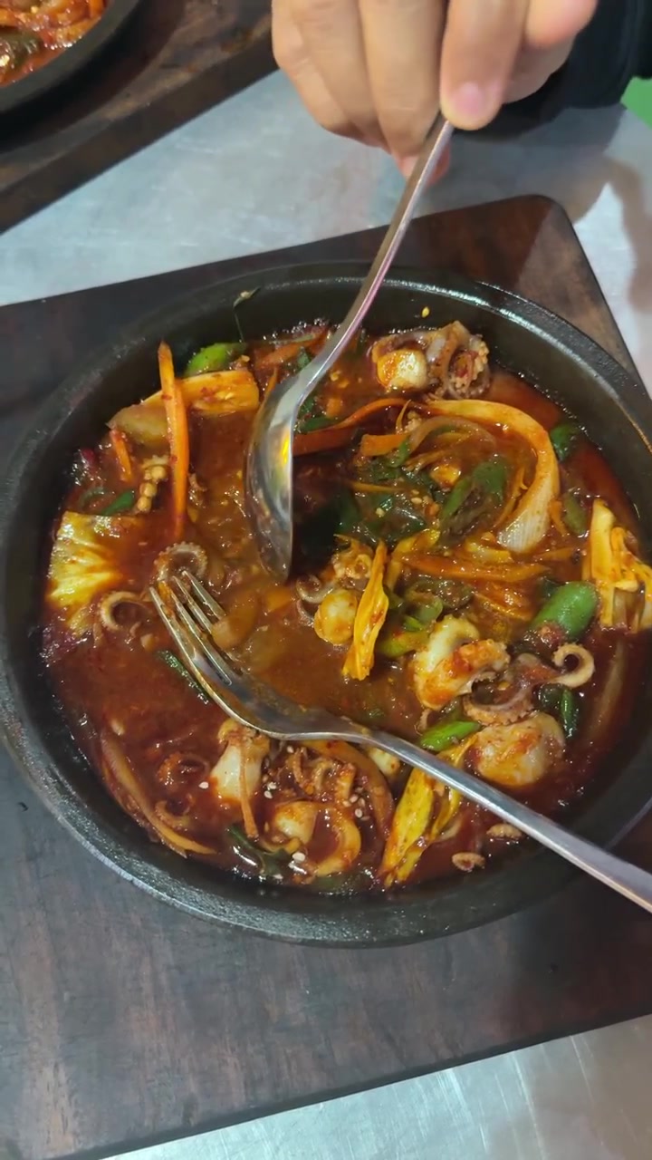Orang Menikmati Gurita Tumis Pedas dalam Mangkuk Batu Panas