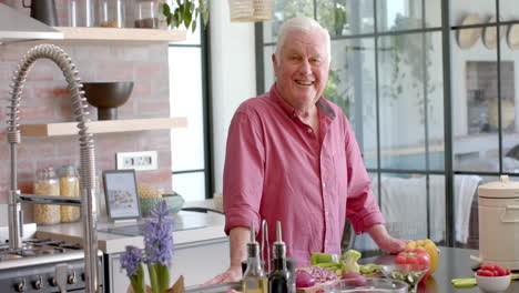 portrait of happy senior caucasian man cooking dinner in kitchen at home, slow motion