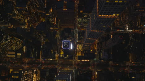 Aerial-birds-eye-overhead-top-down-panning-view-night-city.-Fly-around-tall-modern-skyscraper-towering-above-busy-avenue.-Manhattan,-New-York-City,-USA