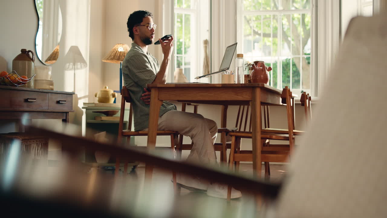 Man Talking on Phone and Typing on Laptop in Home Office