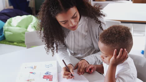 Female-infant-school-teacher-working-one-on-one-with-a-young-schoolboy-in-a-classroom,-elevated-view