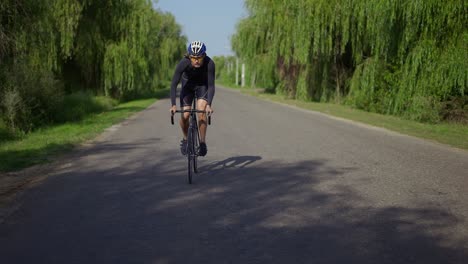 male cyclist in helmet rides bicycle along the track, gaining speed, front view