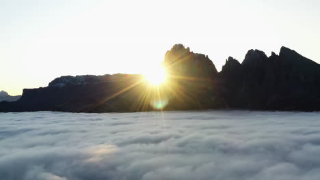 aerial view of the sun disappearing behind silhouette peaks, on a foggy morning