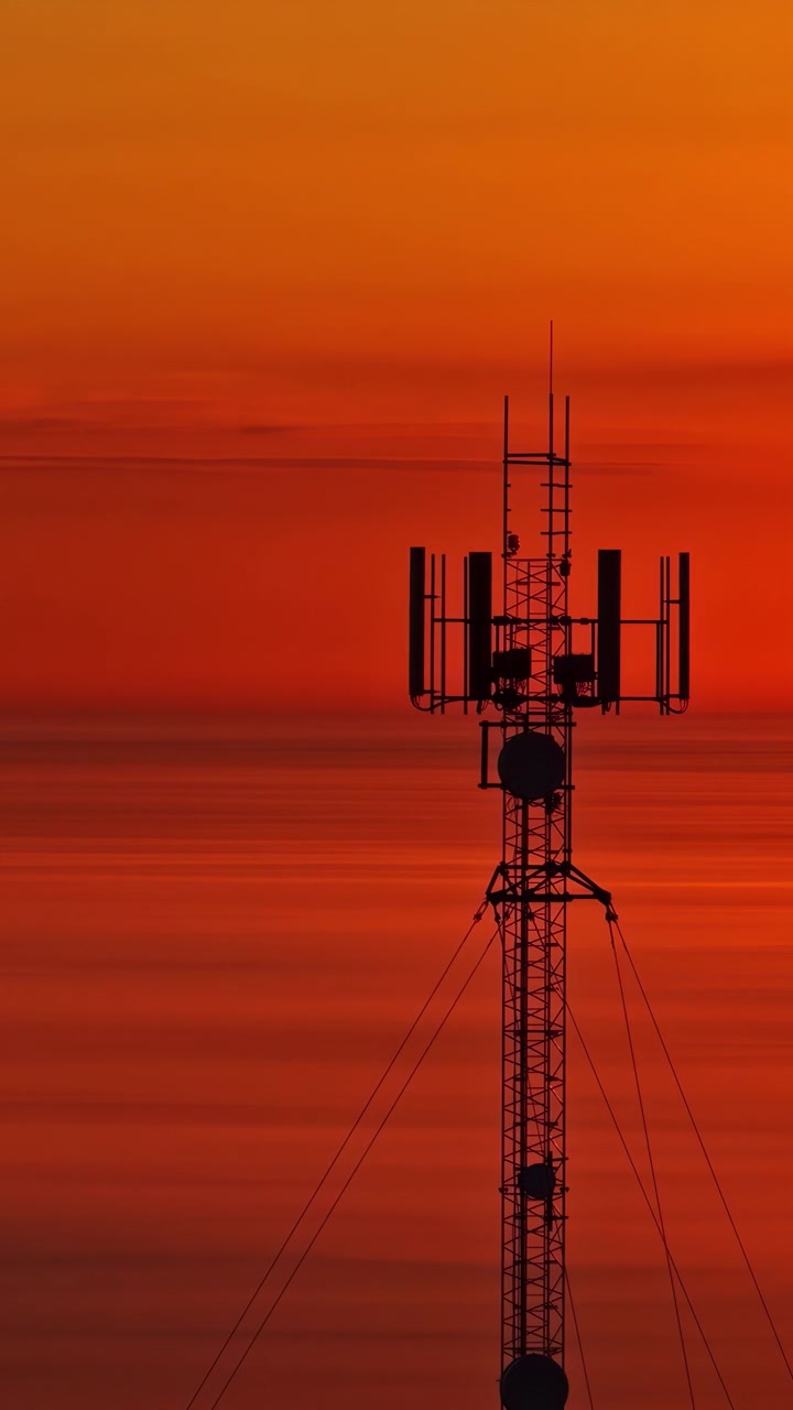 Mobilmast i silhuet mod levende orange solnedgangshimmel, ildevarslende dommedagsforberedelser