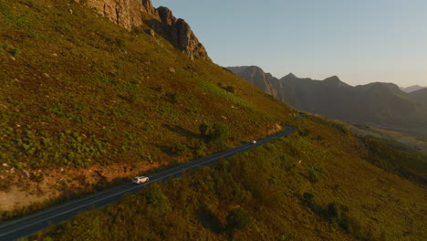 Verfolgung-Von-Autos,-Die-Auf-Der-Straße-Fahren,-Die-Sich-Um-Den-Bergrücken-In-Der-Landschaft-Schlängelt.-Erstaunliche-Landschaft-In-Der-Goldenen-Stunde.-Südafrika