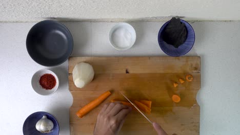 male hands chopping carrots looking down on cutting board in kitchen