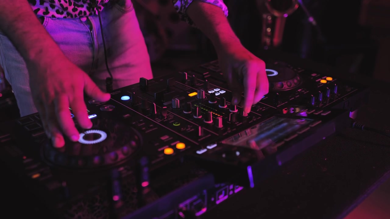 Primo piano delle mani di un DJ che azionano mixer e giradischi in una discoteca.