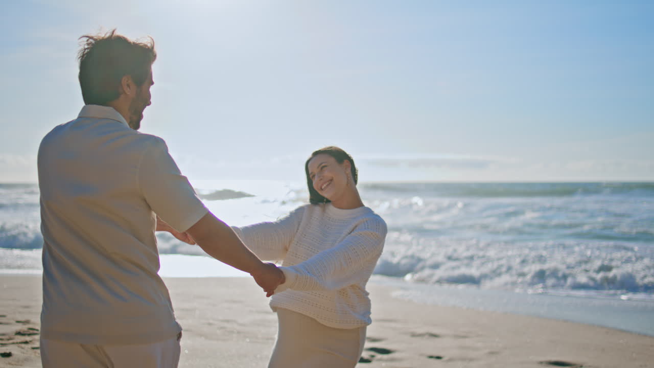 웃는 커플이 해변을 회전하며 아기를 기다리는 동안 사랑을 즐기고 있습니다. 배우자 재미