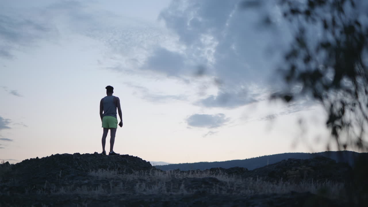 Epic twilight view of man standing on mountain peak, raising hands