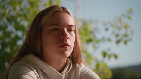 young woman in peaceful outdoor setting with eyes slightly close, lost in thought, as sunlight softly illuminates her face, background shows blurred green leaves