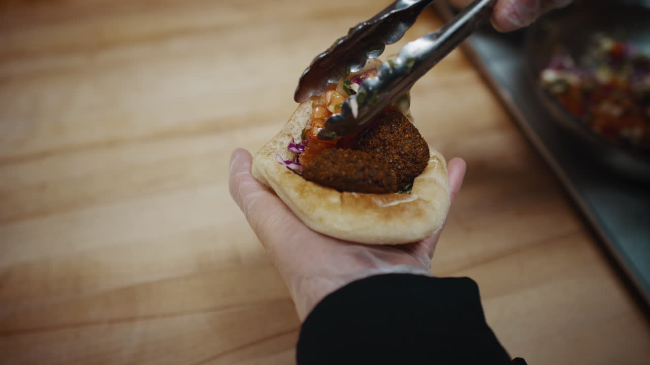 Chef che inserisce verdure e pomodori all'interno di una tasca di pita.