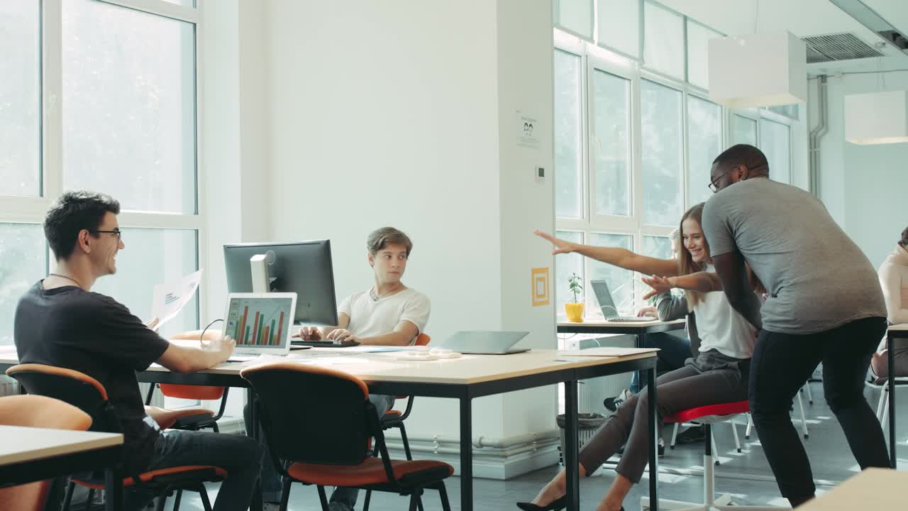 Happy friends moving on chair around coworking. Black man running from office.