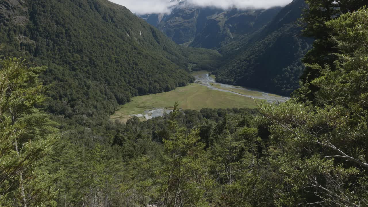 Views of the Routeburn river in a valley in between mountains and forest on a sunny summer day at Routeburn Track, New Zealand.