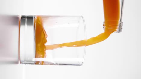 slow motion shot of carrot juice being poured into a glass against a white background