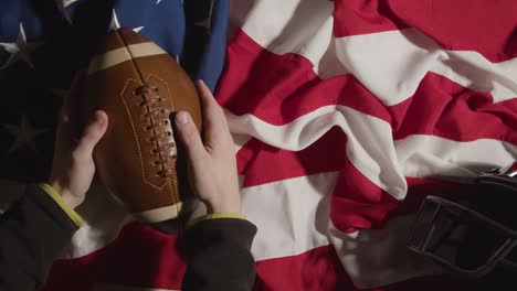 Overhead-Aufnahme-Einer-Person,-Die-American-Football-Auf-Der-Stars-And-Stripes-Flagge-Mit-Helm-Aufhebt