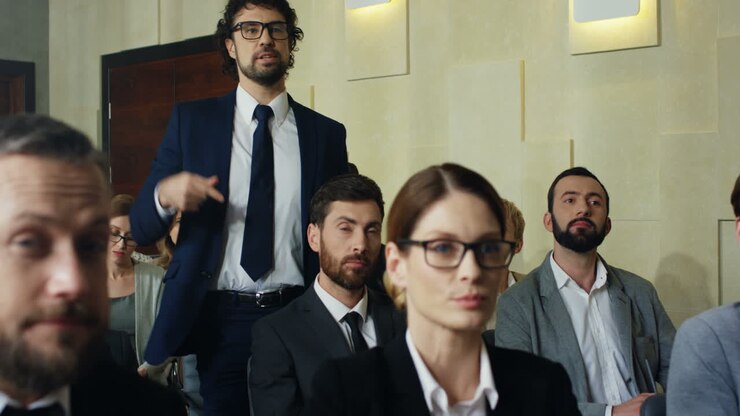 Close-up view of the audience at a business conference listening to the speaker, then caucasian businessman stands up and asks a question