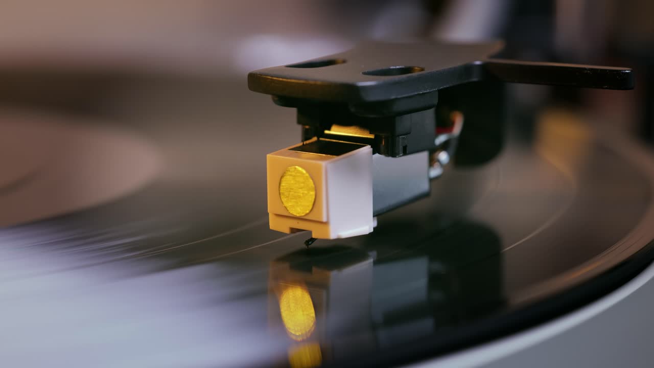 Primo piano dettagliato del braccio di un giradischi con testina bianca, posizionato su un disco in vinile nero sul piatto, che evidenzia la precisione delle apparecchiature audio