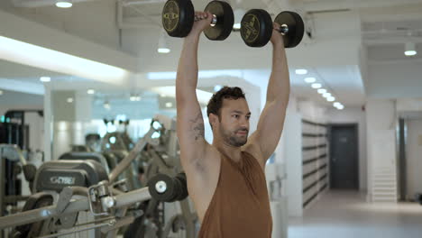 medium shot of fit athlete performing dumbbell shoulder press, standing in gym