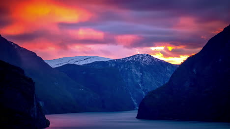 brilliant sunset pink and purple clouds cross the sky above steep mountainsides plummeting into a misty fjord in scandinavia - time lapse