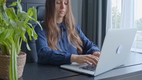 joven mujer caucásica trabajando en una computadora portátil en una oficina gris moderna, en cámara lenta