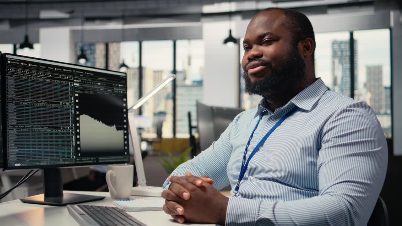 Smiling portfolio manager at computer desk evaluates assets based on statistics