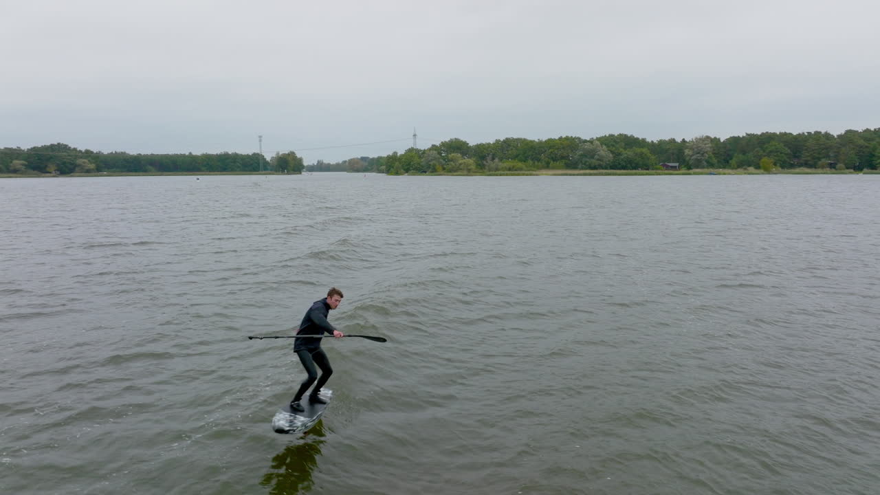 하이드로 수프 포일 (hydro sup foil) 의 운동 선수가 강에서 파도에서 서핑하고, 드론으로 촬영되어 근접합니다.