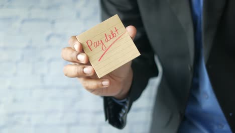 man holding a sticky note with "pay debt" written on it