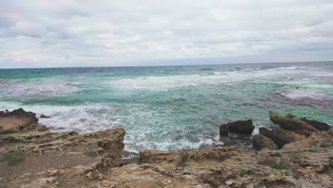 Olas-Turbulentas-Chocan-Contra-Rocas-Escarpadas-En-La-Costa,-Bajo-Un-Cielo-Nublado,-Creando-Un-Paisaje-Marino-Dinámico