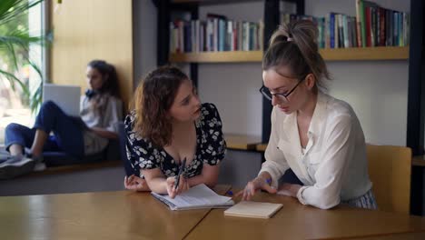 Two-adult-female-students-discussing-new-project-in-library