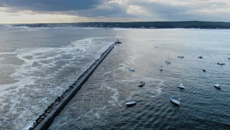 Aerial-View-Of-Eastern-Point-Lighthouse-At-The-Pier-In-Gloucester,-Massachusetts-With-Sailboats-Adrift-On-The-Ocean-During-Sunset---orbiting-drone-shot