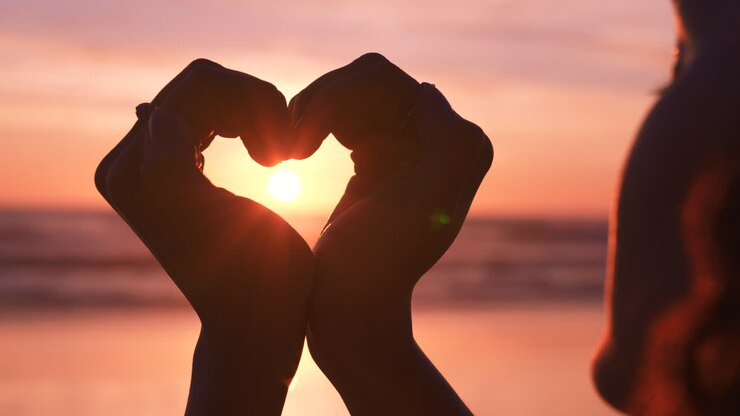 Spiaggia, cuore e mani per amore al tramonto