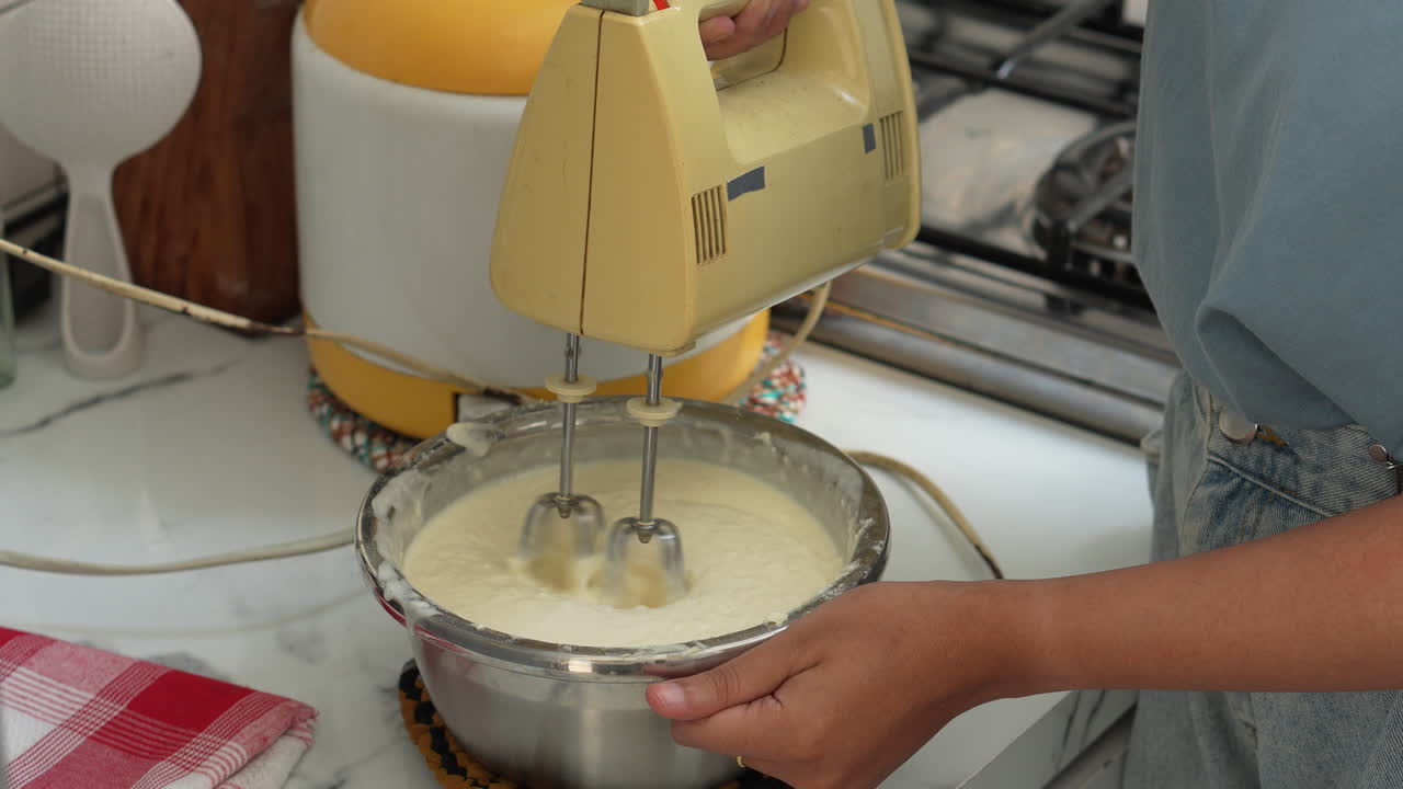manos de mujer batendo crema para pastel de tiramisu usando mezclador de mano eléctrico en la mesa de la cocina