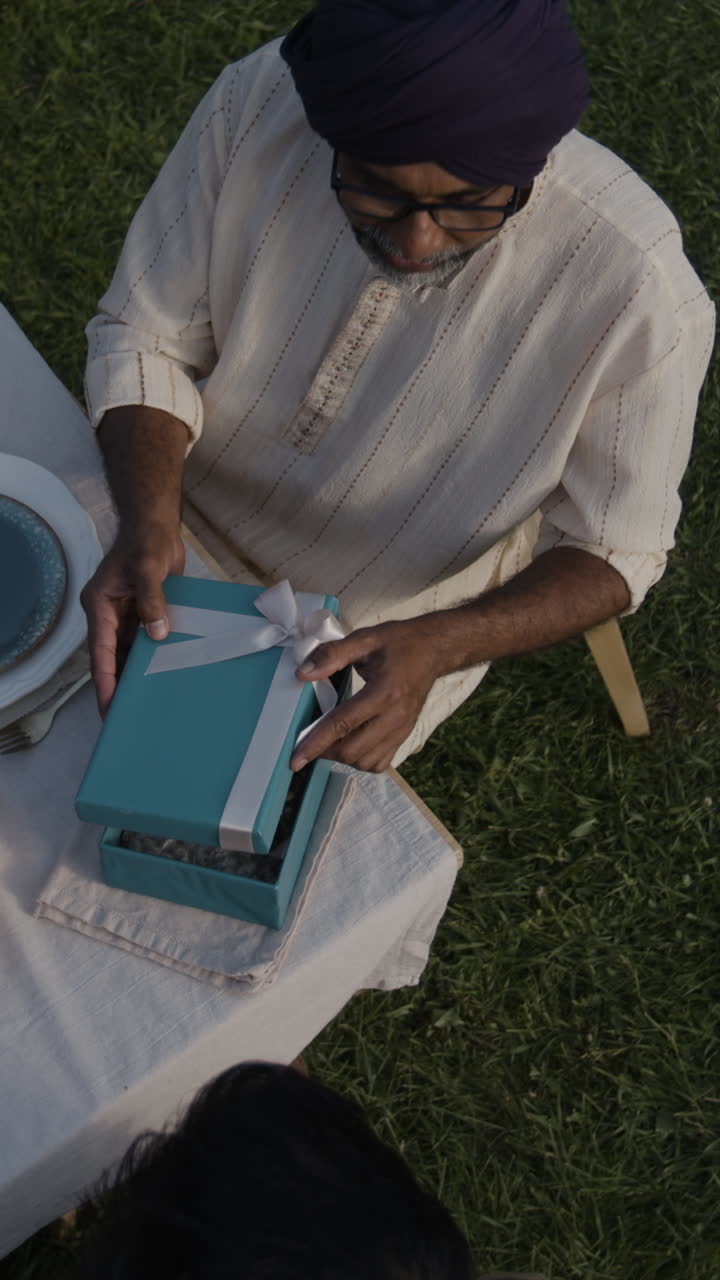 Man Opening a Gift Box with Small Jars at an Outdoor Gathering
