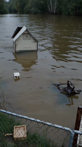 submerged shed and chair in murky floodwaters