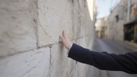 man walking through the ancient streets of jerusalem's old city, connecting with its history by touching the weathered stone walls