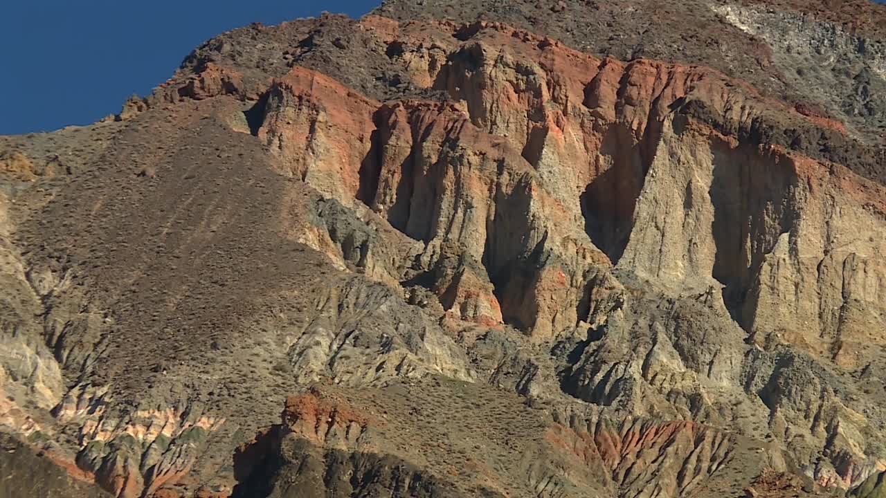 Close up view of steep eroded cliffs featuring orange, tan, and gray striated rock formations in Death Valley National Park, California, USA