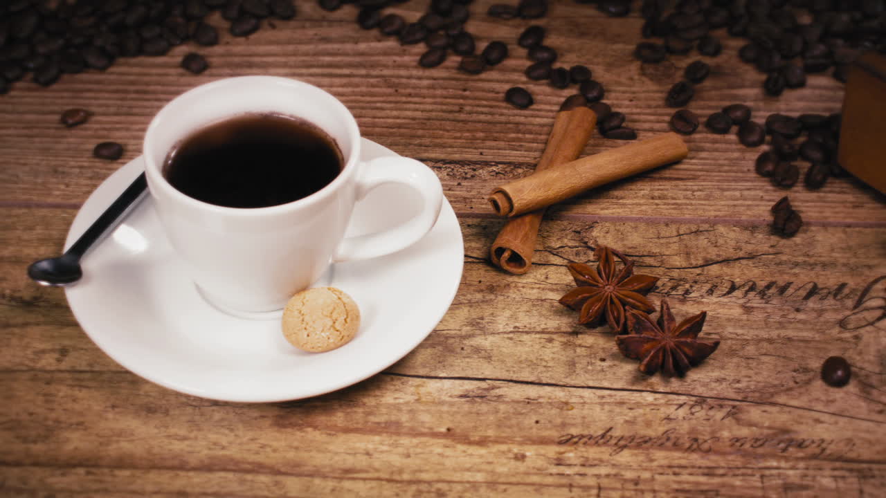 Nærbillede af en lækker lille kaffe med kanel, stjerneanis og kaffebønner på et træbord.