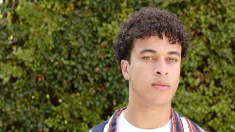 biracial man standing in front of hedge outdoors, slow motioncopy space