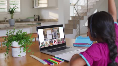 Schoolgirl-using-laptop-for-online-lesson-at-home,-with-diverse-teacher-and-class-on-screen