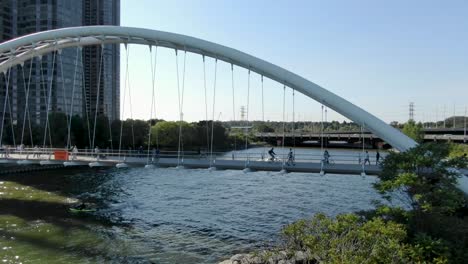 aerial shot flying away from sunny toronto bridge on lake ontario with pedestrians and cyclists on it