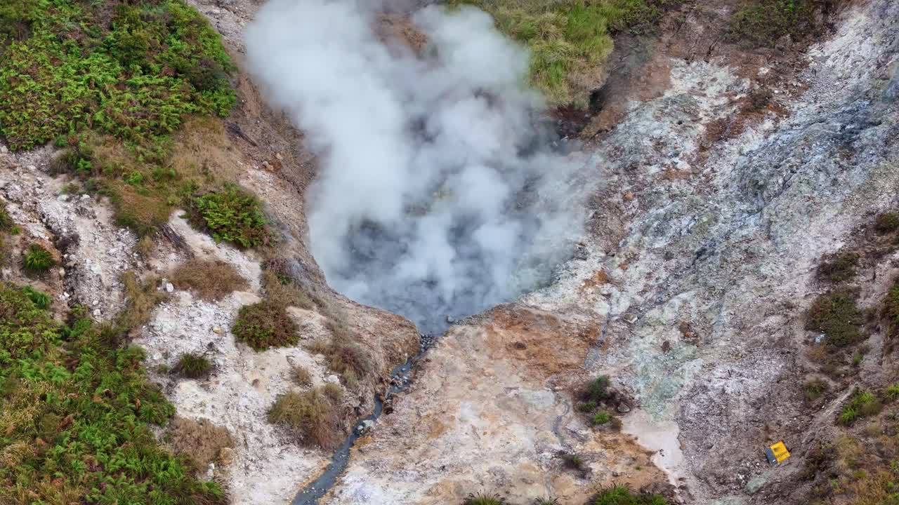 Drone video of hot steam rising from a sulfur-rich crater, surrounded by rocky hills and patches of green vegetation in a volcanic region. Sikidang Crater, Dieng, Indonesia