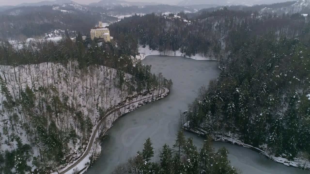 foto reveladora de un lago congelado rodeado de bosque y un castillo de cuento de hadas en la distancia en invierno